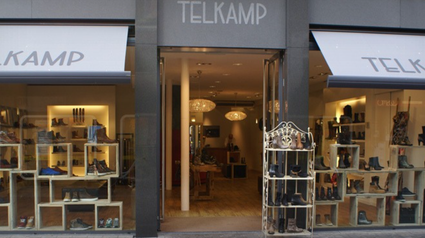 Speciaalzaak Telkamp Schoenen Woerden, provincie Utrecht, Groene Hart, entree van de schoenenwinkel in het centrum met verlichte etalages, houten presentatiemeubels en collectie dames- en herenschoenen.