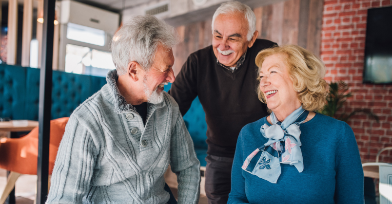 Oudere dame en twee oudere heren praten en lachen met elkaar