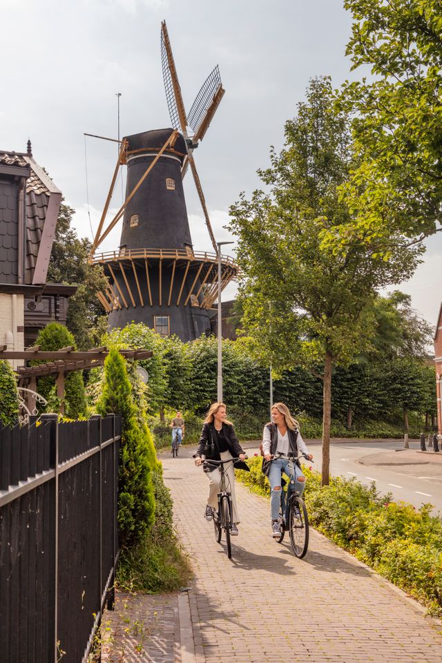Korenmolen De Windhond in Woerden, Groene Hart, met fietsers op een fietspad langs de historische stellingmolen. Populaire fietsroute door de vestingstad met cultureel erfgoed, recreatief fietsen en bezienswaardigheden in het Groene Hart en Utrecht.