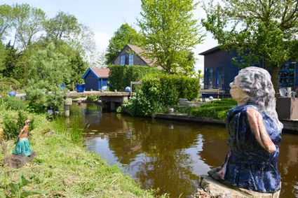 Vakantiehuis De Blauwe Meije in Zegveld, Groene Hart, sfeervolle vakantiewoning aan een smalle waterloop met bruggetje, weelderige tuin en kunstwerken in het landelijke polderlandschap.