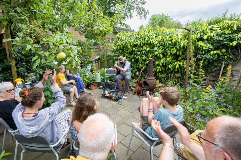 Huiskamerfestival Gluren bij de Buren, met een intiem liveoptreden van een gitarist in een groene achtertuin voor publiek van verschillende leeftijden. Foto: Rick de Visser.