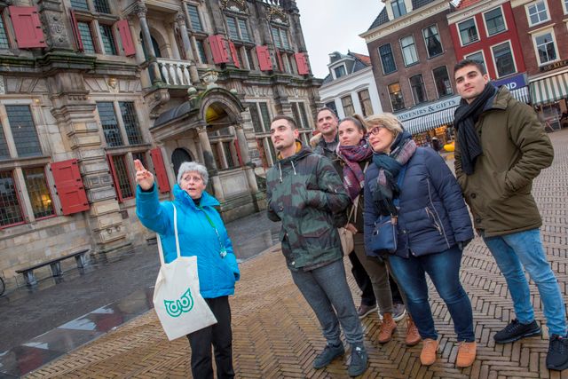 Groep mensen die uitleg krijgt tijdens een Vermeer wandeling naast het Stadhuis in het Centrum van Delft