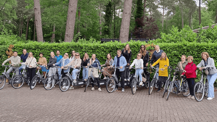 Groep fietsers staan op een rijtjes voor groene haag, klaar voor vertrek