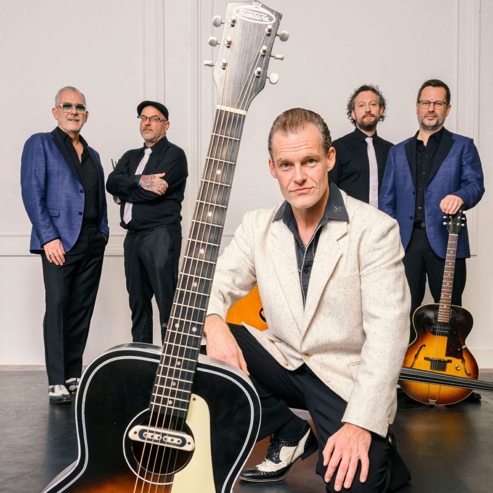 Foto van de band, 5 heren met hun muziekinstrumenten in blauw-zwart-wit gekleed, voor een lichte achtergrond.