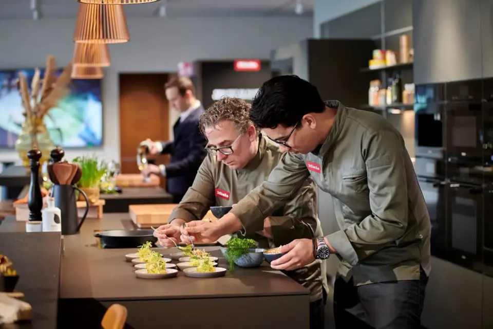 Personen volgen een kookworkshop en kijken naar gerechten op het aanrecht.