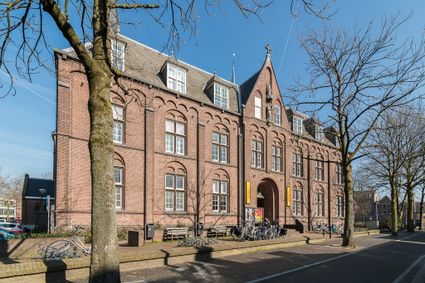 Cultureel centrum Het Klooster, Woerden, Groene Hart, historisch bakstenen gebouw met hoge ramen, entreeboog, fietsenrekken en bomen langs de straat in het stadscentrum.