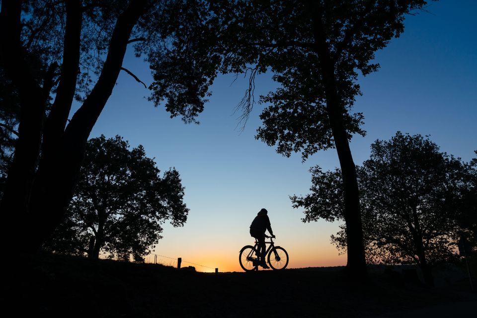 Man fietst op zijn ebike door een open natuurgebied. De zon is bijna onder