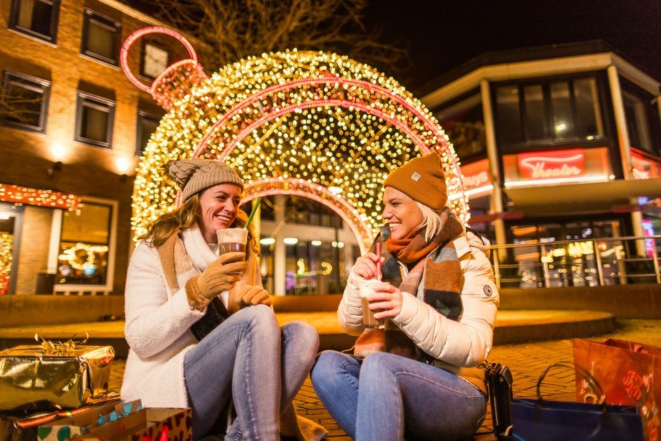 Twee vrouwen in winterjassen en met wanten aan drinken een kop warme chocolademelk in het centrum van Emmeloord