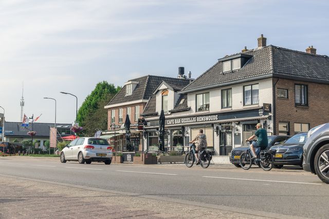 Straatbeeld in het centrum van Renswoude met Café Bar Gezellig Renswoude, andere horecazaken, fietsers en geparkeerde auto's. De foto laat de horeca en levendigheid van de dorpskern zien.