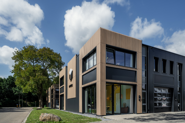 Een foto van de voorgevel van de locatie met een blauwe lucht met een aantal witte wolken.