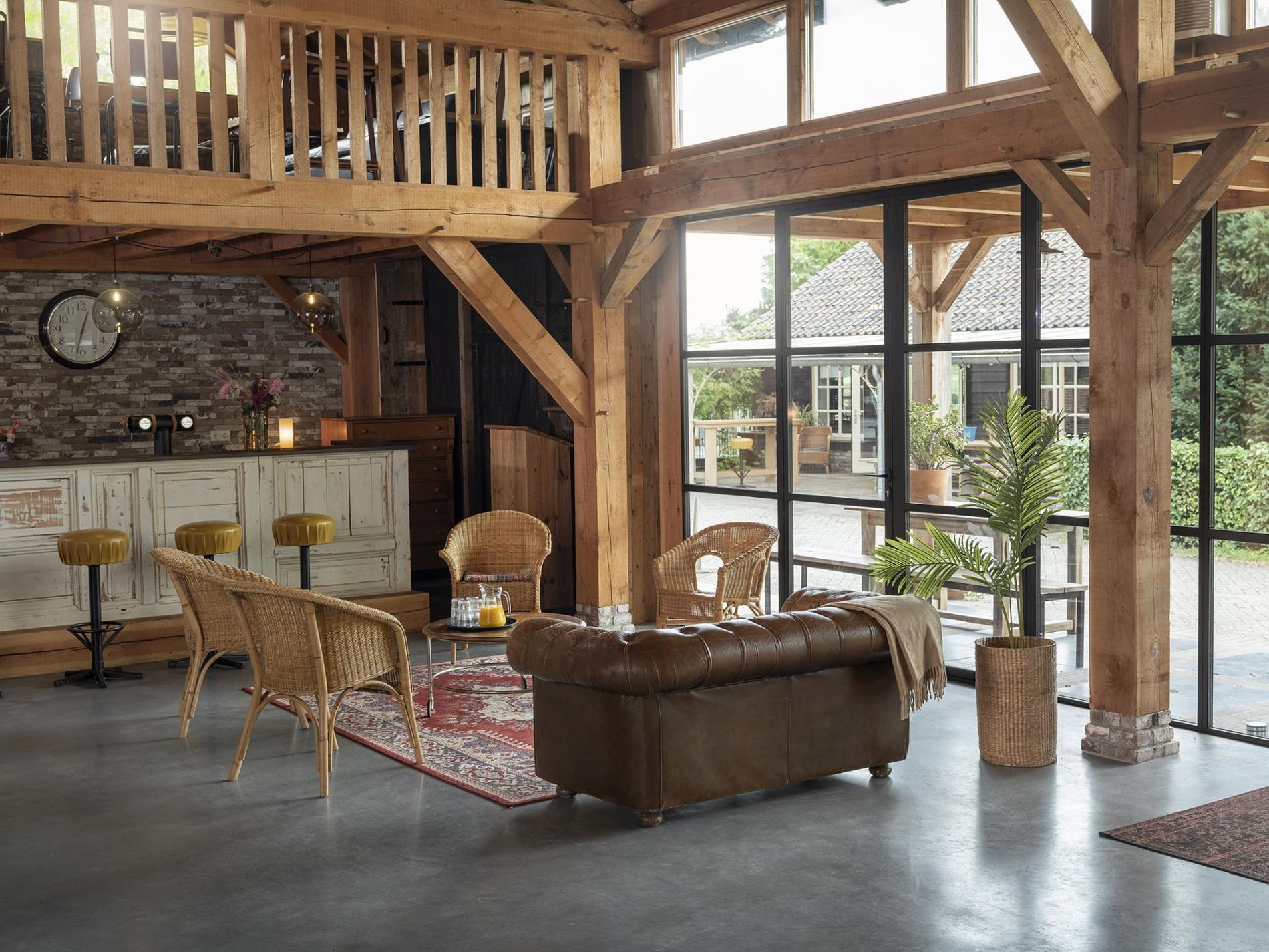 Hoge zaal met houten balken en spanten in het zicht, openslaande deuren, een bar en een zithoek.