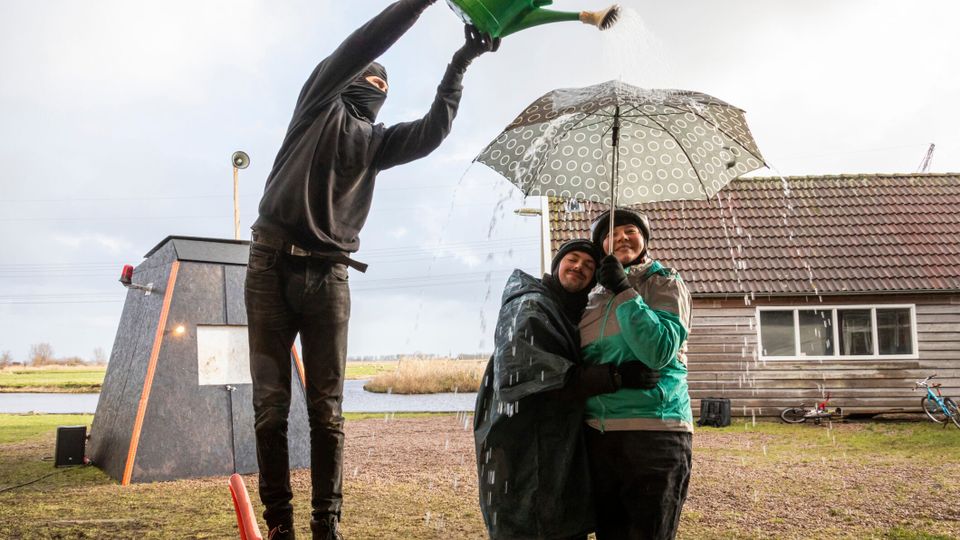 Iemand die water gooit over 2 mensen met een paraplu