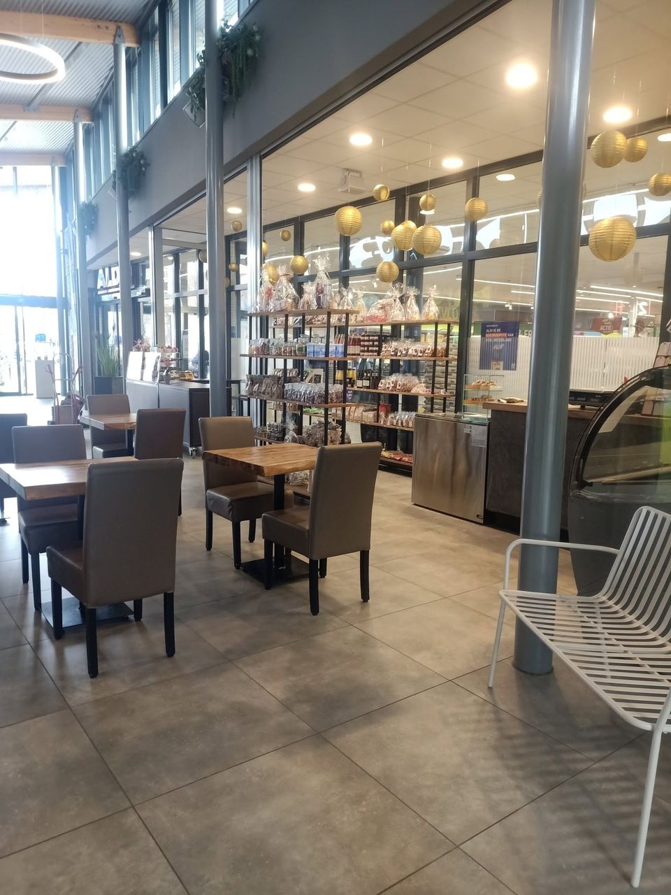 Binnenterras met tafels en stoelen, op de achtergrond schappen met producten en cadeau pakketten.
