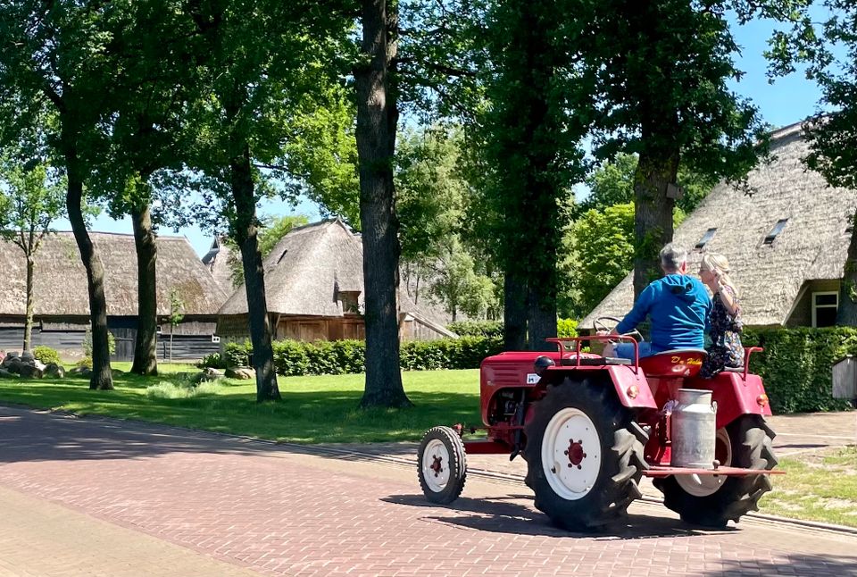 Twee mensen rijden op een oldtimer tractor door Gees.