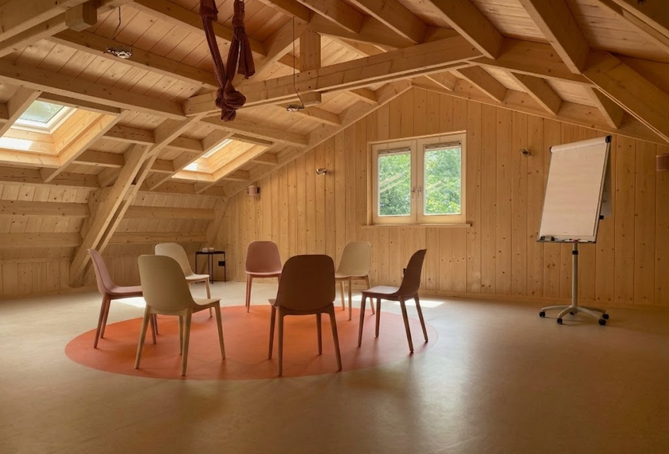 Sfeervolle vergaderruimte van Aliedas Annex bij Esti Yoga in Lopik, Groene Hart, met houten balkenplafond, dakramen, stoelen in een kring en flip-over voor bijeenkomsten.