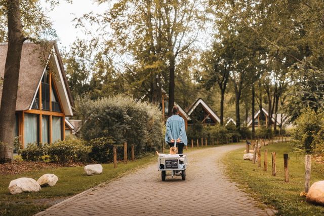 Eine Frau läuft mit einem Kind im Bollerwagen hinter sich her über einen Ferienpark in Drenthe.