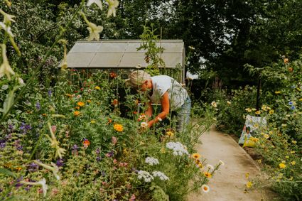 Een vrouw staat in een moestuin vol met bloemen