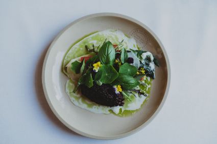 Bord met daarop een gerecht van diverse bloemen en groene bladeren in een licht groene saus.