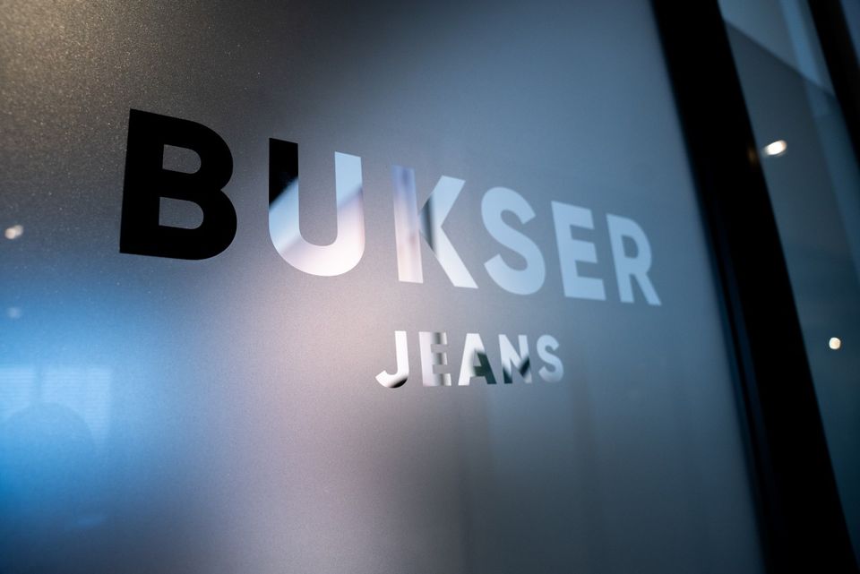 Jeanswinkel Busker Jeans in Woerden, Groene Hart, close-up van het logo op een glazen wand als herkenbaar detail van het winkelinterieur.