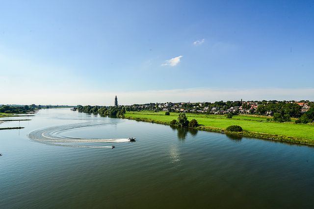 Een boot vaart over de Nederrijn. Op de achtergrond zie je groen gas met de skyline van Rhenen en de Cuneratoren.