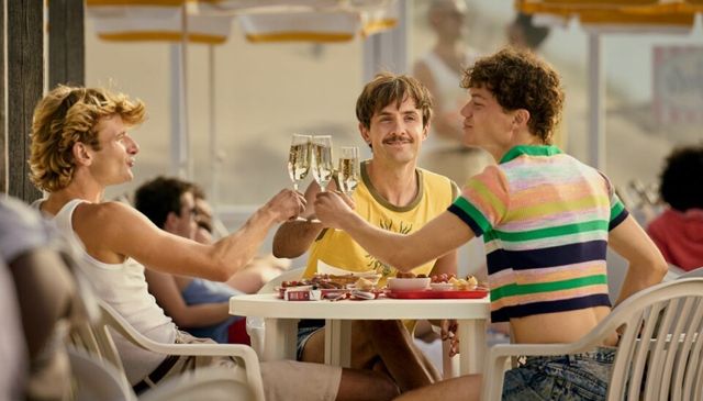 drie vrienden zitten samen op het terras en heffen het glas met elkaar