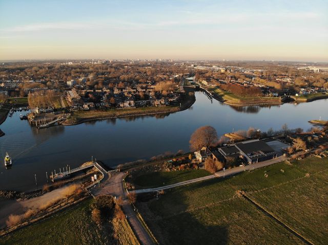 Dronefoto vanuit de lucht, op de foto zijn huizen, water en een weiland te zien.