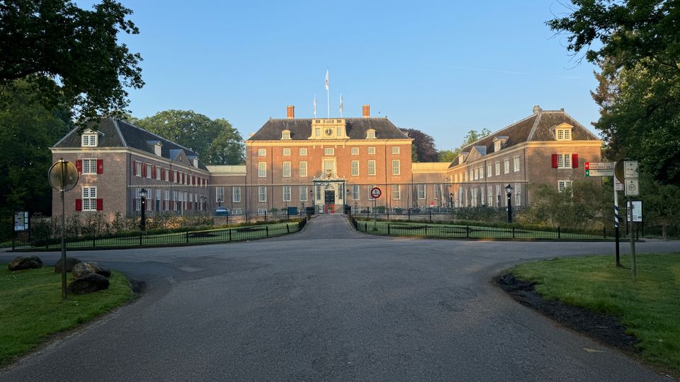 De voorkant van Slot Zeist, een imposant gebouw met een blauw hek en een gracht eromheen