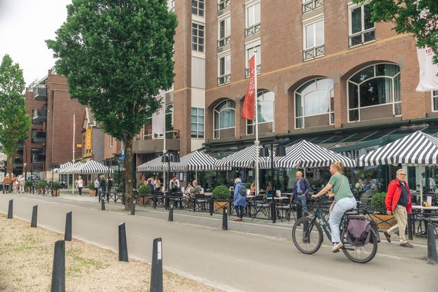 Straatbeeld in het centrum van Zeist met terrassen, winkels, voetgangers en een fietser. De foto laat de levendige en gastvrije sfeer van de dorpskern van Zeist zien.