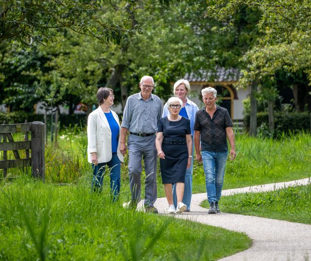 Vrijwilligers van Logeerhuis Bredius wandelen samen over een groen pad in het Brediuspark in Woerden, omringd door natuur en bomen.