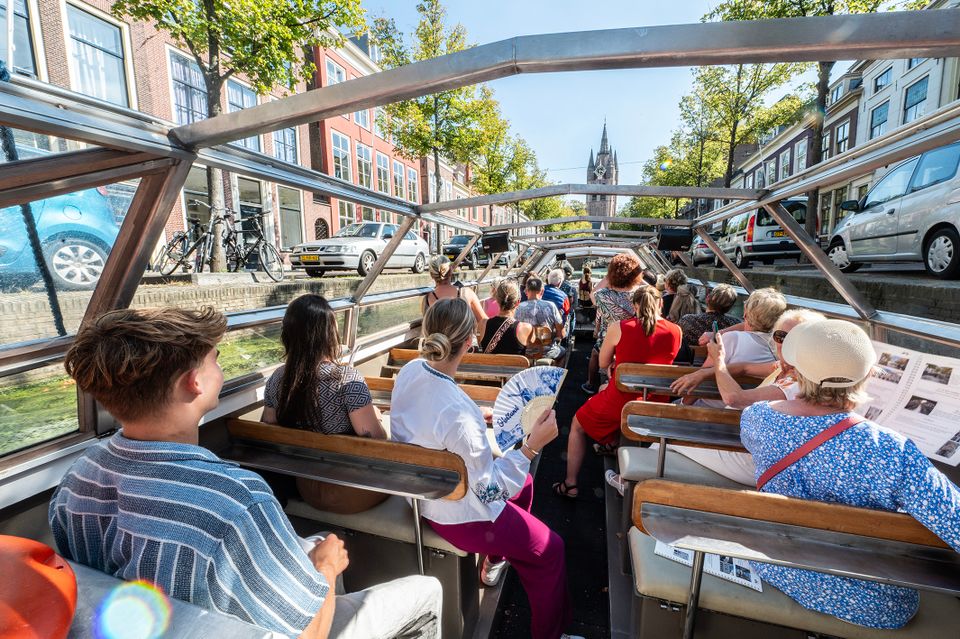 Mensen zitten op een zomerdag in een rondvaartboot in Delft en varen richting de Oude Jan