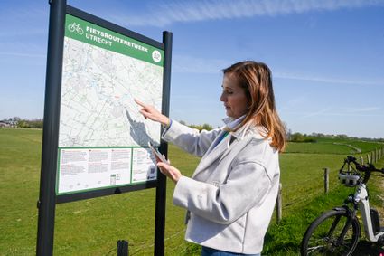 Dame met fiets kijkt op informatiepaneel fietsroutenetwerk