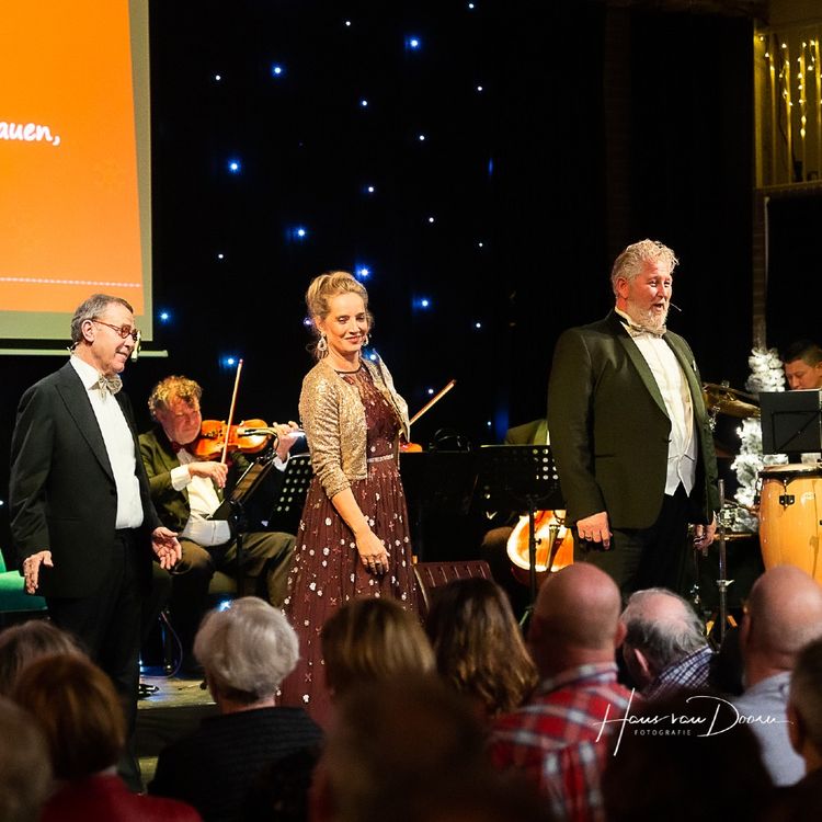 Foto van het orkest met op de voorgrond een zangeres en twee zangers.