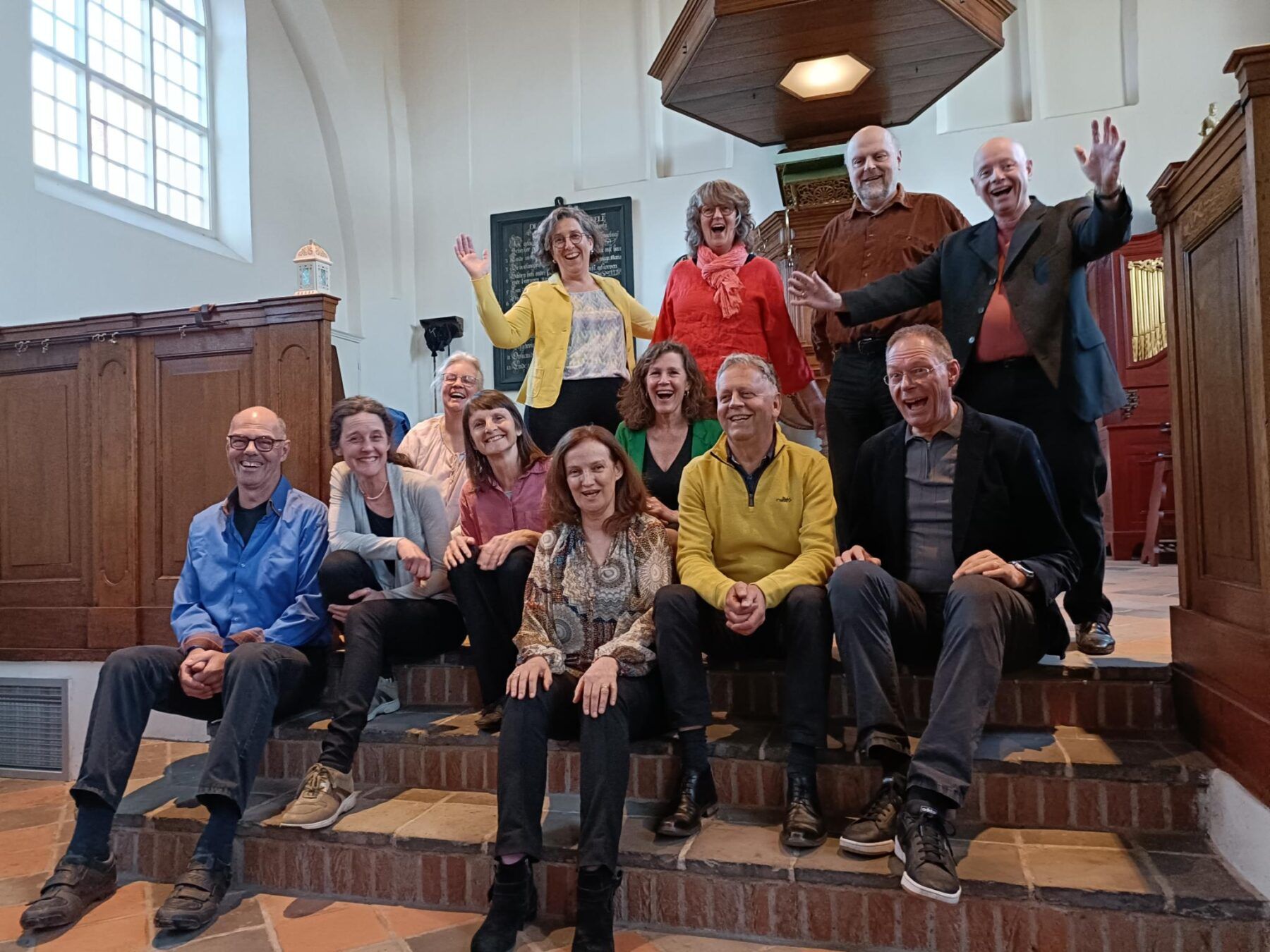 De 12 leden van zangensemble Innervoice zitten op de trap in het Lodewijkskerkje