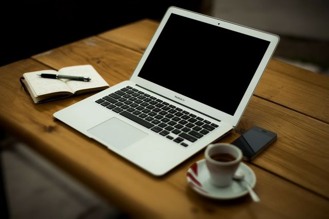 Een laptop op een tafel met notitieboekje en een kopje koffie.