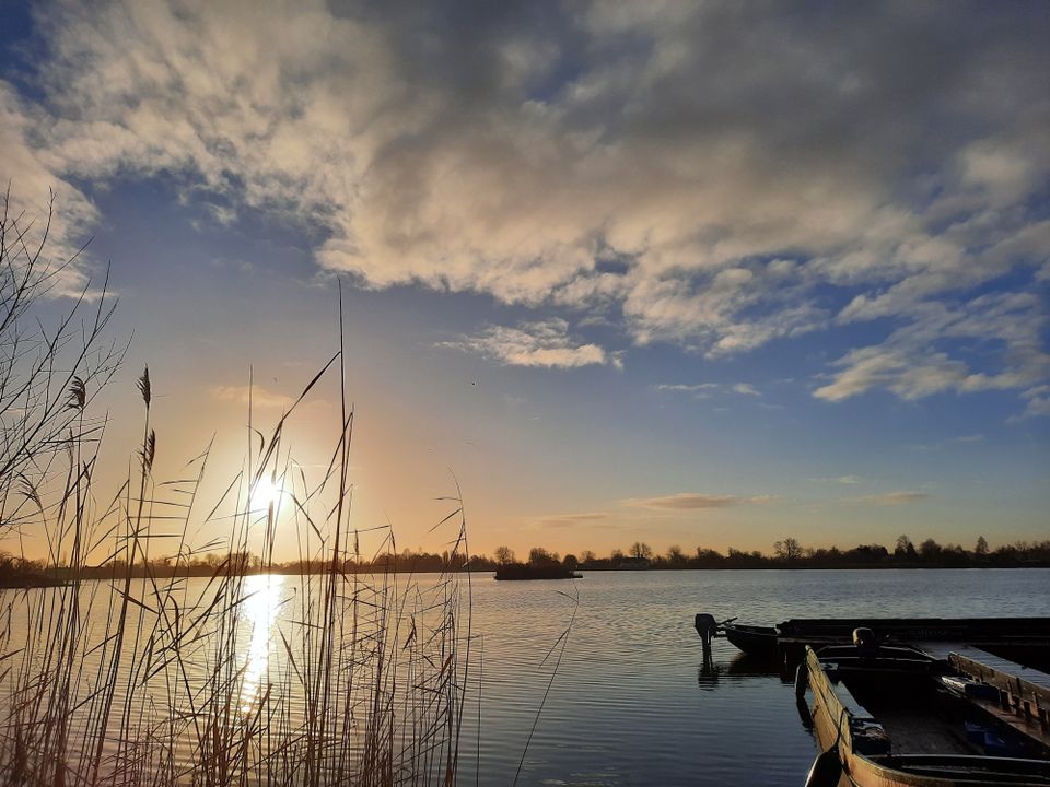 Natuurgebied Reeuwijkse Plassen bij Reeuwijk, Groene Hart, zonsondergang boven het water met riet in de voorgrond en aangemeerde bootjes langs een steiger in een Hollands veenplassengebied.