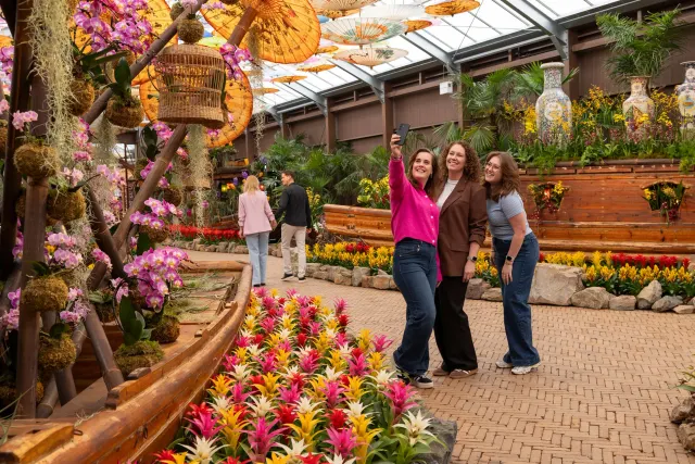 Vrouwen die samen een selfie maken tussen mooie bloemen en een stel die achter hen loopt.