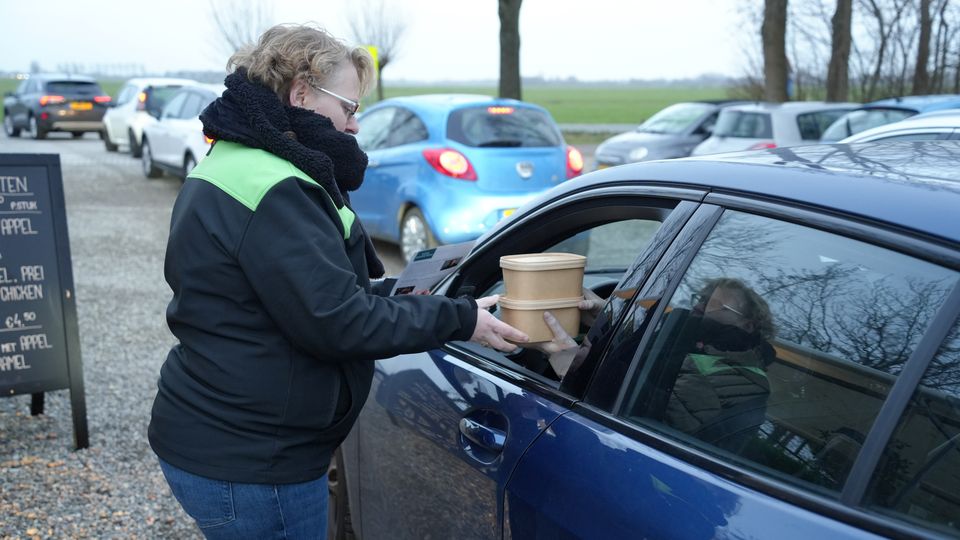 Medewerker overhandigt een afhaalmaaltijd aan een automobilist tijdens een drive-through bij Kameryck