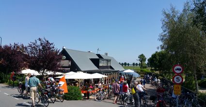 Restaurant De Strooppot in De Hoef, Groene Hart. Druk terras aan het water met fietsers, geparkeerde fietsen en bezoekers tijdens een zonnige fietstocht door de regio.