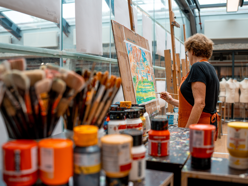 UITvergroot een vrouw met een oranje schort die schildert bij De Vak