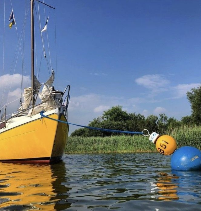 Gele zeilboot ligt aangemeerd aan een MarBoei.