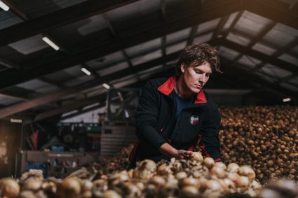 Man in zwart vest staat in een opslag bij een berg met witte uien en kijkt geconcentreerd naar de uien