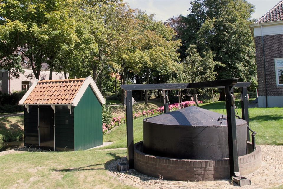 Groen klein huisje met agrarische machine op het land.