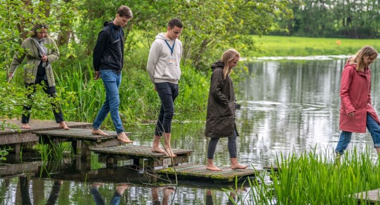 Groep mensen loopt op blote voeten over het blotevoetenpad bij De Boerinn in Kamerik, omgeven door groen en water in het Groene Hart.