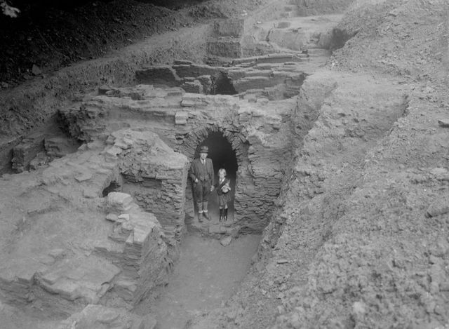 Een man en een kind staan in een opgegraven pannenoven, 1942. Zwart-wit foto.