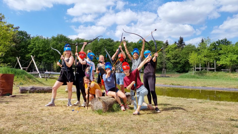 Groep mensen met helmen op en pijl en boog in hun handen poseren voor de foto.