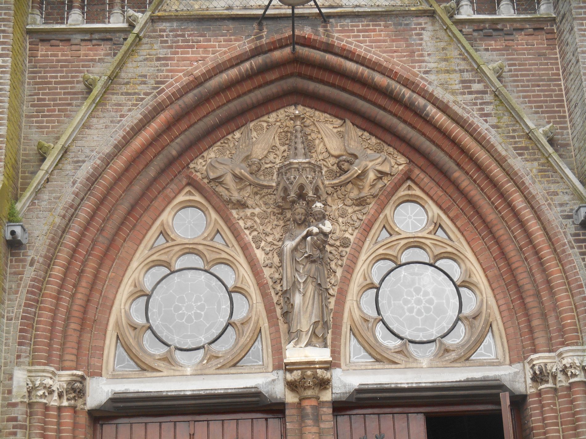 Een gotische boog van steen met Maria en kind. Links en rechts kleine roos venstertjes