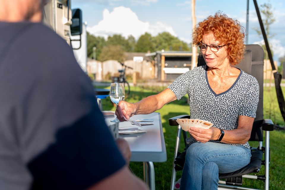 2 toeristen die op hun kampeerplekje bezig zijn met een kaartspel in de namiddagzon.