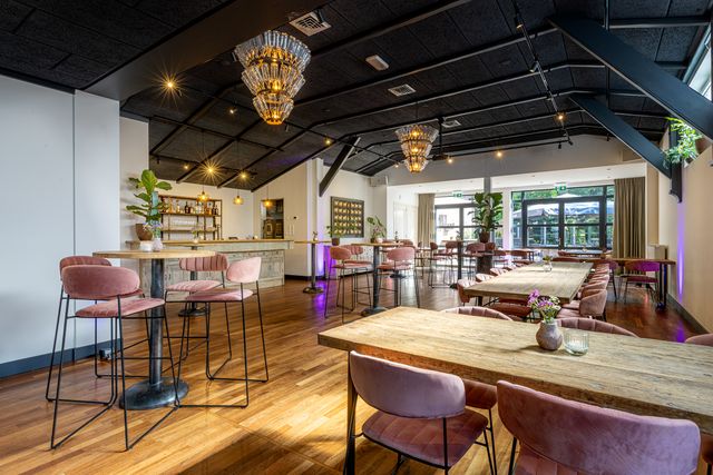 Sfeervolle binnenruimte van Diemer Event Locatie met houten vloeren, roze fluwelen stoelen, grote kroonluchters en een stijlvolle bar met warme verlichting.