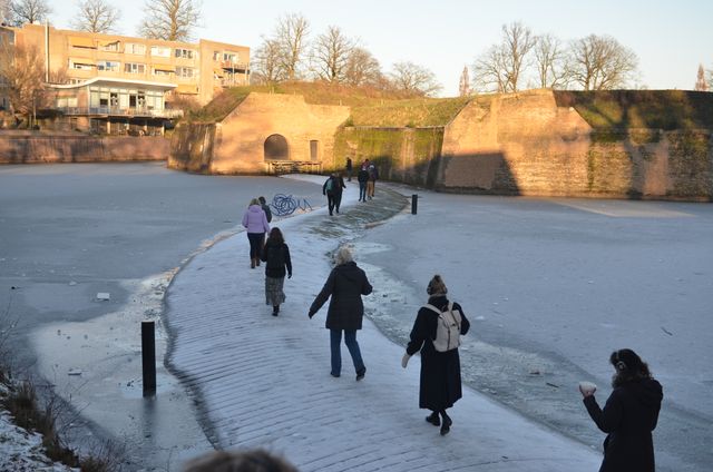 Mensen lopen een voor een over een bruggetje bedekt met sneeuw