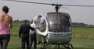 Mensen lopen naar stilstaande helikopter op grasveld.